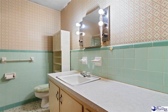 bathroom with vanity, toilet, tile walls, wallpapered walls, and a wainscoted wall