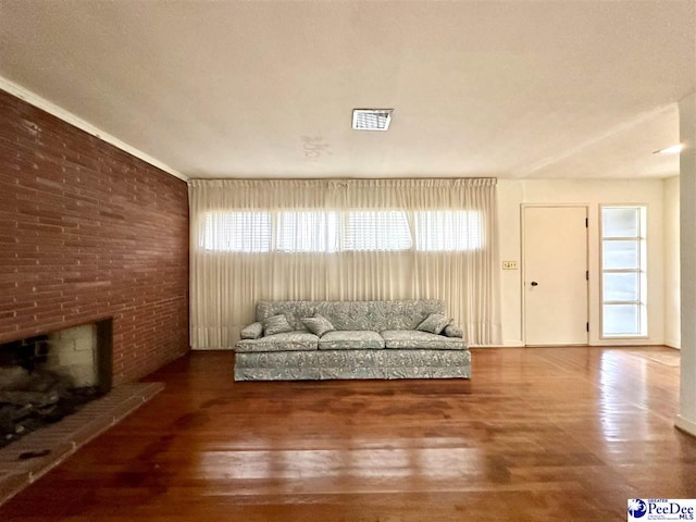 unfurnished living room with brick wall, wood-type flooring, and a brick fireplace