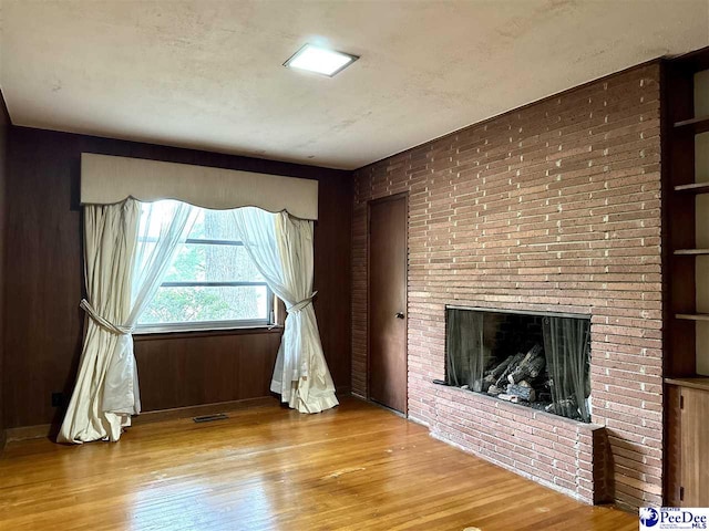 unfurnished living room with wooden walls, a fireplace, and light hardwood / wood-style floors