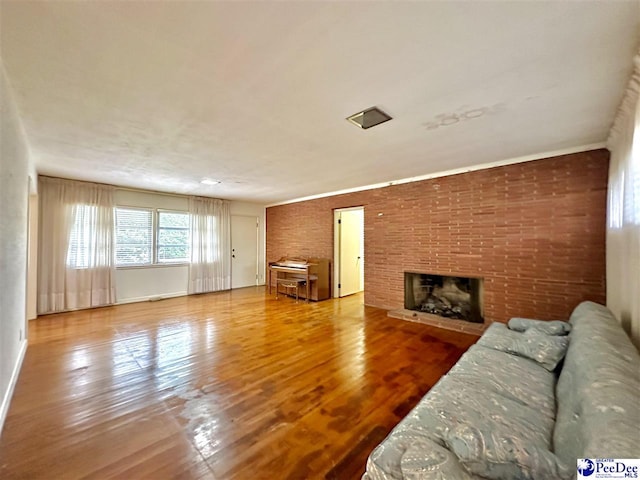 unfurnished living room featuring hardwood / wood-style flooring, ornamental molding, brick wall, and a fireplace