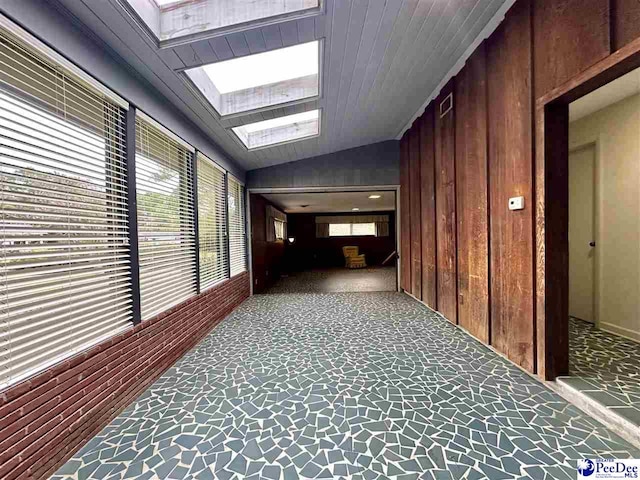 hallway with carpet flooring, lofted ceiling with skylight, and wood walls