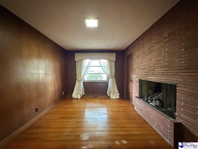 unfurnished living room with wood-type flooring and a brick fireplace