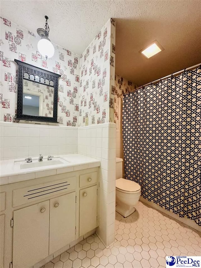 bathroom with tile patterned floors, toilet, tile walls, a textured ceiling, and vanity