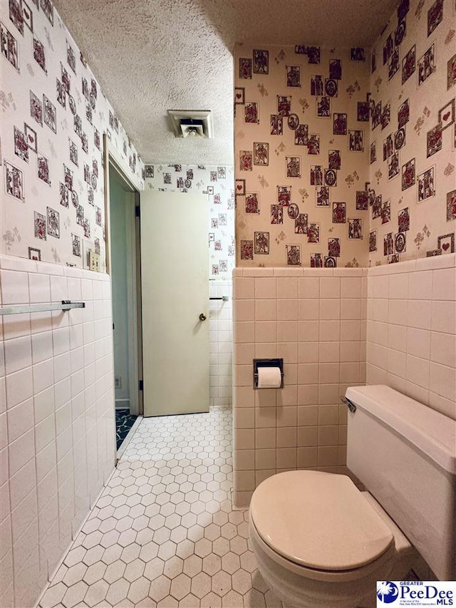 bathroom featuring tile walls, tile patterned flooring, toilet, and a textured ceiling