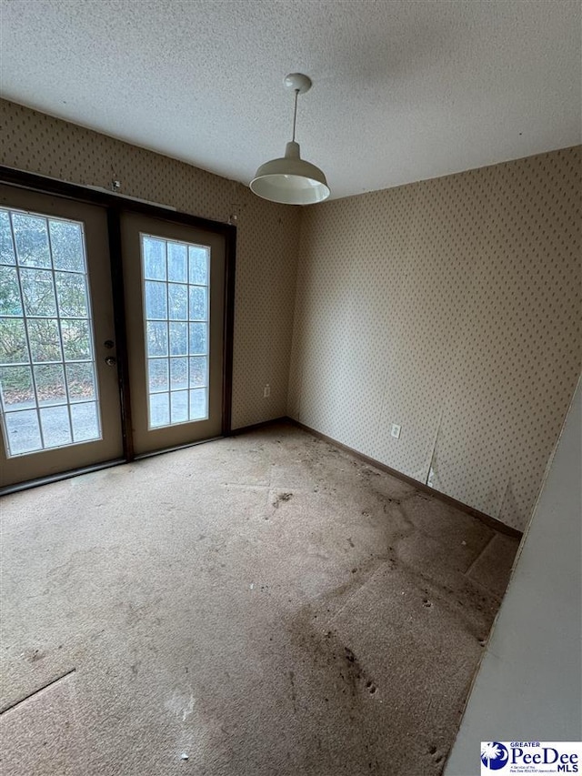 carpeted empty room featuring a textured ceiling and wallpapered walls