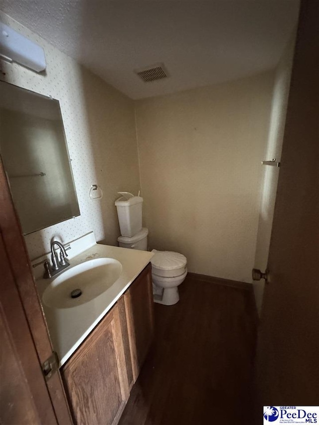 half bath with visible vents, toilet, wood finished floors, baseboards, and vanity