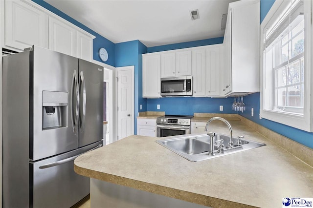 kitchen featuring appliances with stainless steel finishes, white cabinets, light countertops, and a sink