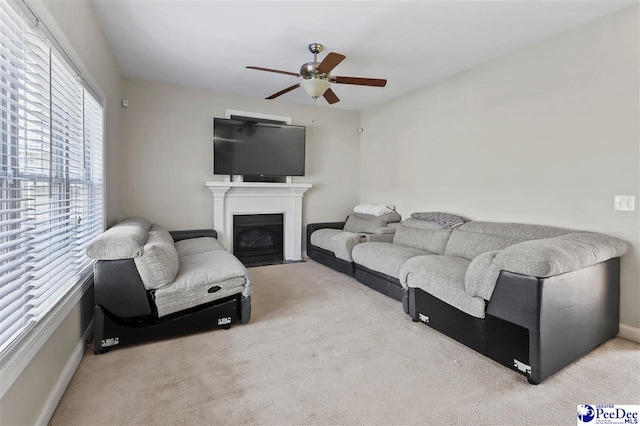 living room featuring a fireplace with flush hearth, light carpet, ceiling fan, and baseboards