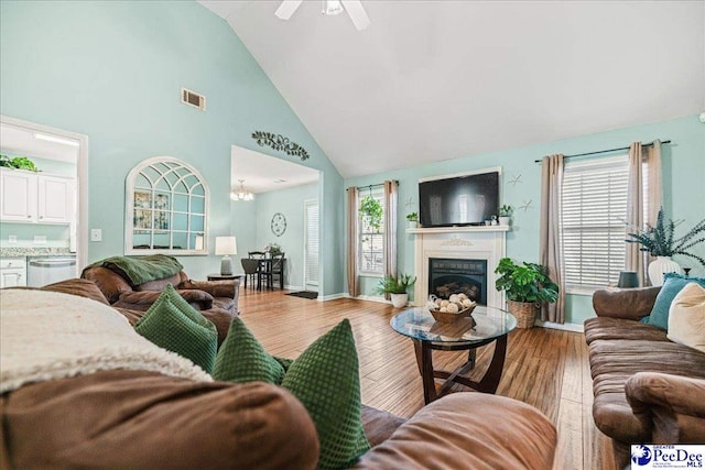 living area featuring a fireplace, visible vents, light wood-style floors, ceiling fan, and high vaulted ceiling