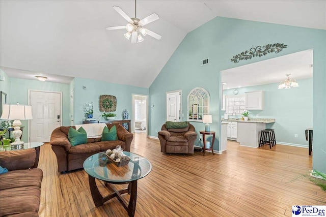 living room with visible vents, light wood-style floors, a ceiling fan, high vaulted ceiling, and baseboards