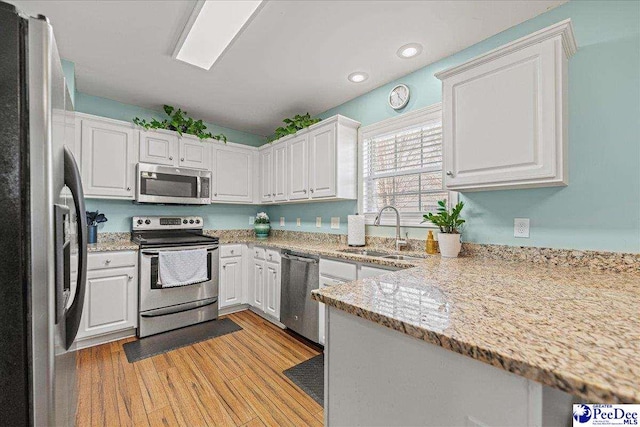 kitchen with light stone countertops, appliances with stainless steel finishes, white cabinets, and a sink