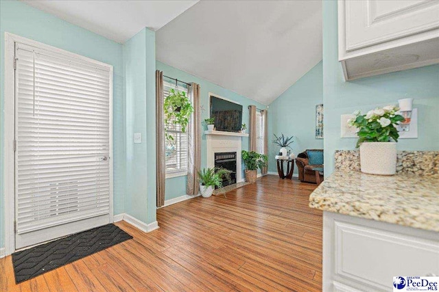 foyer entrance featuring a fireplace with flush hearth, vaulted ceiling, light wood-style flooring, and baseboards