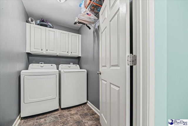 washroom featuring stone finish flooring, washer and clothes dryer, cabinet space, and baseboards