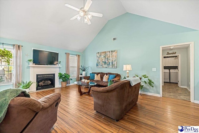 living area with high vaulted ceiling, separate washer and dryer, a fireplace, and wood finished floors