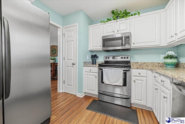 kitchen featuring stainless steel appliances, white cabinets, light wood-style flooring, and light stone counters