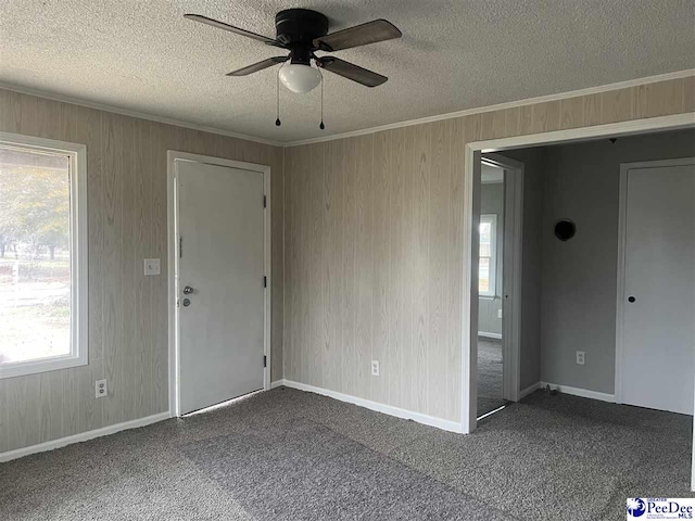 carpeted spare room featuring crown molding, baseboards, wood walls, a textured ceiling, and a ceiling fan