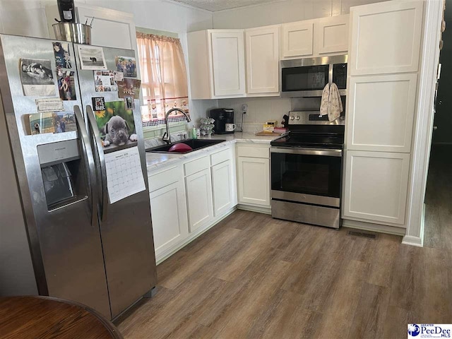 kitchen featuring appliances with stainless steel finishes, dark hardwood / wood-style flooring, sink, and white cabinets