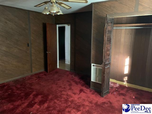 unfurnished bedroom featuring ceiling fan, wooden walls, and carpet floors