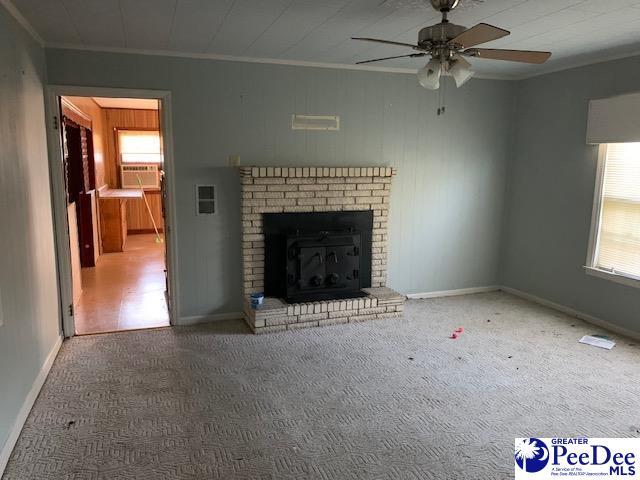 unfurnished living room with a brick fireplace, crown molding, plenty of natural light, and carpet flooring