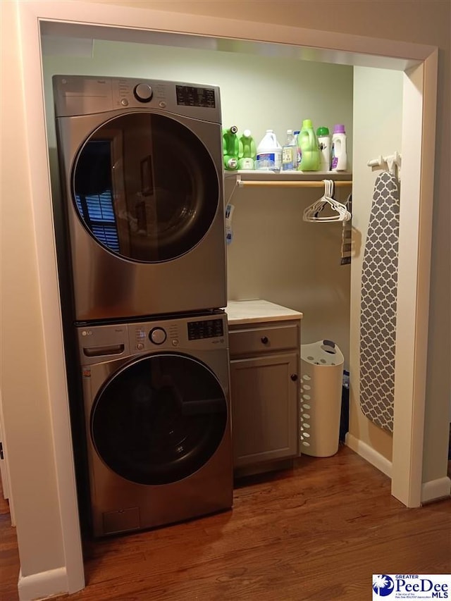 laundry room with cabinets, stacked washer / drying machine, and dark wood-type flooring