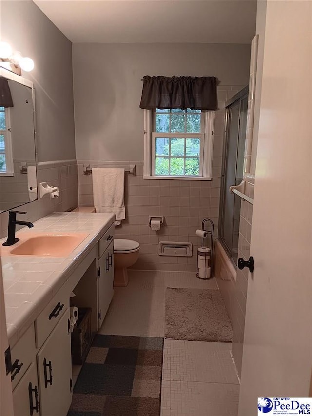 full bathroom with combined bath / shower with glass door, tile patterned flooring, tile walls, vanity, and toilet