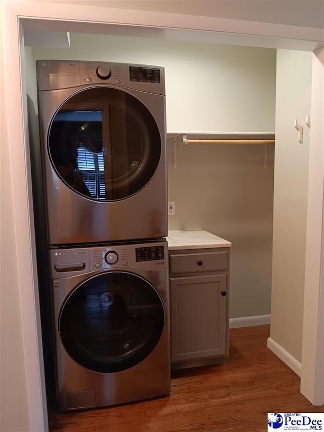 washroom with cabinets, wood-type flooring, and stacked washer and clothes dryer