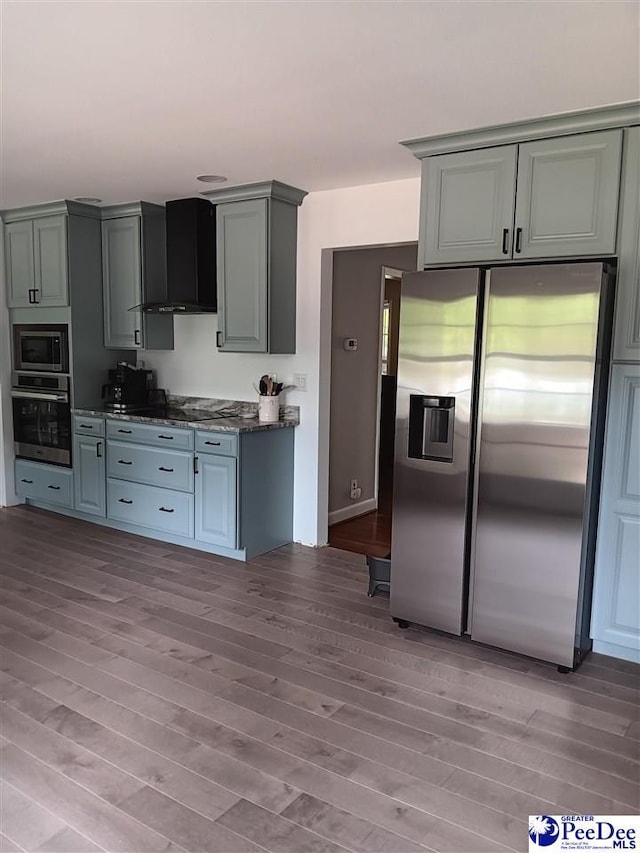 kitchen featuring gray cabinets, appliances with stainless steel finishes, wall chimney range hood, and light hardwood / wood-style floors