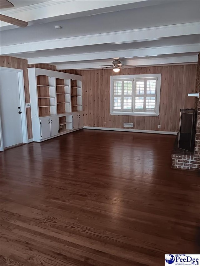 unfurnished living room with dark wood-type flooring, ceiling fan, beam ceiling, and wood walls