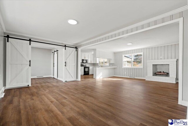 unfurnished living room with wood-type flooring, ornamental molding, and a barn door