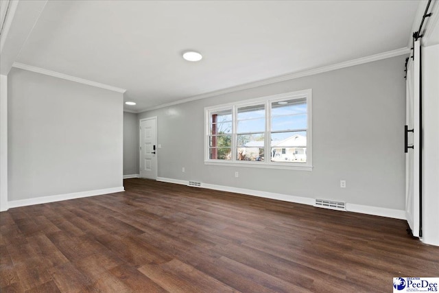 spare room featuring crown molding, dark hardwood / wood-style floors, and a barn door