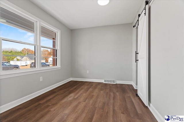 unfurnished bedroom featuring a barn door and dark wood-type flooring