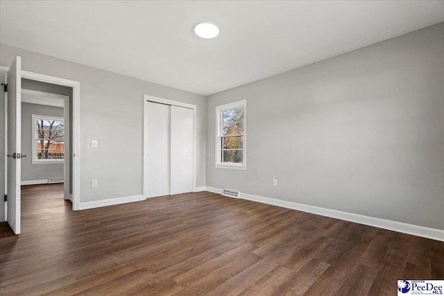 unfurnished bedroom featuring multiple windows, a closet, and dark hardwood / wood-style floors