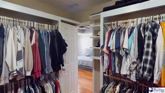 walk in closet with visible vents, wood finished floors, and ceiling fan