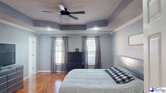 bedroom with ornamental molding, a textured ceiling, a raised ceiling, and wood finished floors