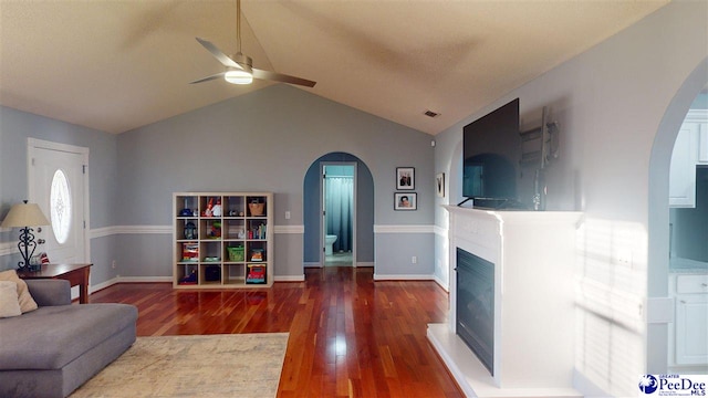 living room featuring arched walkways, wood finished floors, vaulted ceiling, ceiling fan, and a fireplace