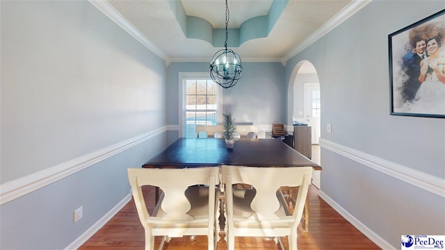 dining room featuring arched walkways, an inviting chandelier, wood finished floors, and a raised ceiling