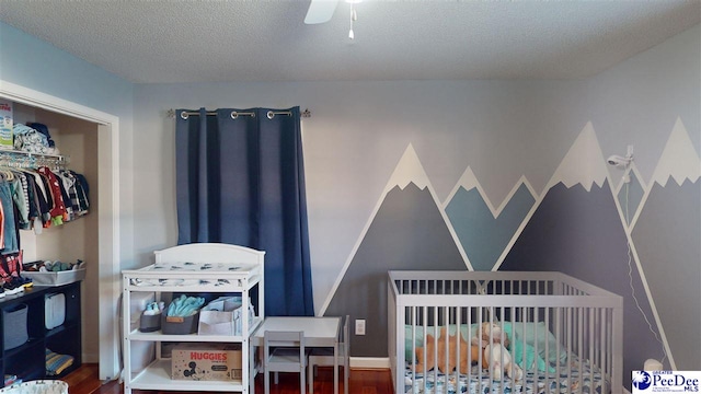 bedroom featuring wood finished floors, ceiling fan, a textured ceiling, and a nursery area