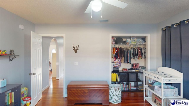 bedroom with a textured ceiling, visible vents, a closet, arched walkways, and wood finished floors