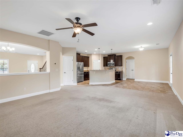 unfurnished living room featuring ceiling fan with notable chandelier and light carpet