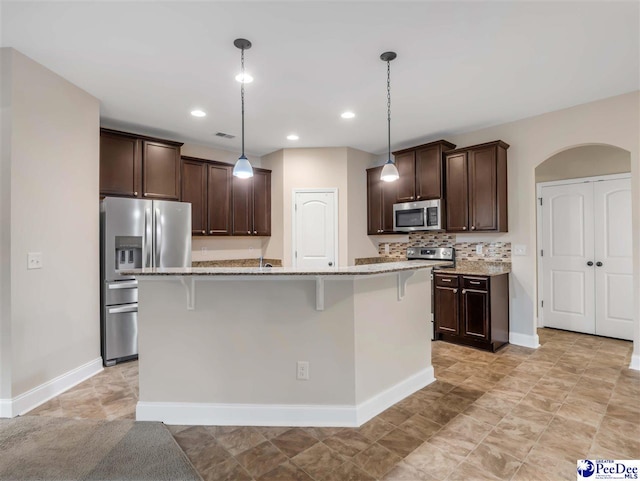 kitchen featuring an island with sink, a breakfast bar area, hanging light fixtures, dark brown cabinetry, and stainless steel appliances