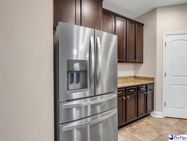 kitchen with light stone counters, dark brown cabinetry, stainless steel fridge, and light tile patterned floors