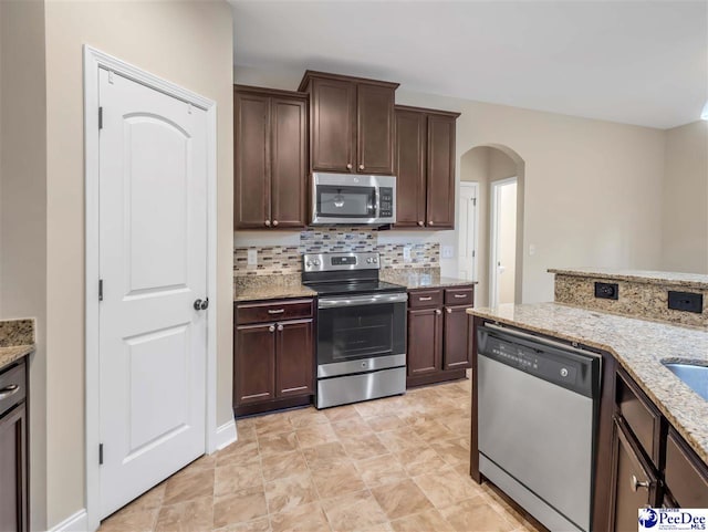 kitchen featuring dark brown cabinetry, light stone countertops, decorative backsplash, and stainless steel appliances