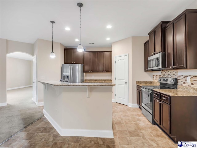 kitchen with hanging light fixtures, appliances with stainless steel finishes, a kitchen breakfast bar, light stone countertops, and backsplash