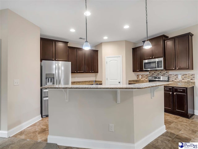 kitchen with appliances with stainless steel finishes, decorative light fixtures, a breakfast bar area, and a center island with sink