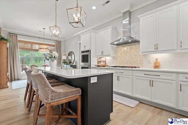 kitchen featuring visible vents, a chandelier, ornamental molding, a sink, and wall chimney range hood