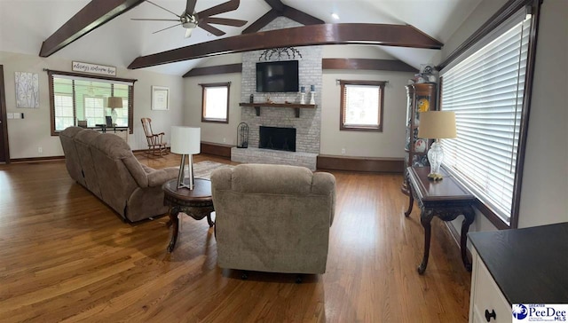 living area with lofted ceiling with beams, a ceiling fan, a brick fireplace, wood finished floors, and baseboards