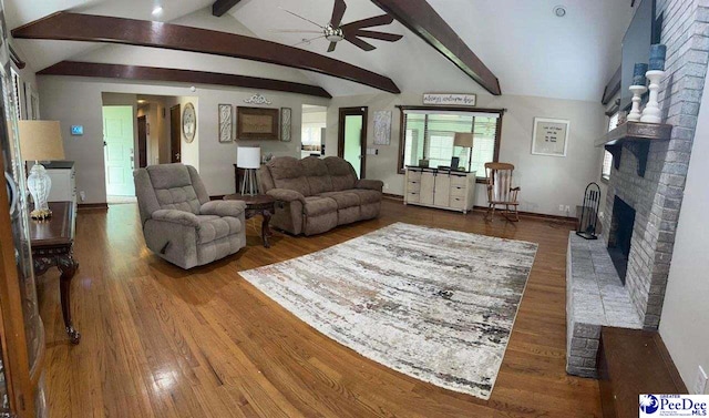 living area featuring vaulted ceiling with beams, a fireplace, and wood finished floors