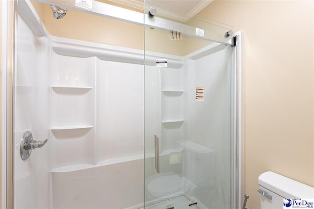 bathroom featuring toilet, ornamental molding, and a shower with shower door