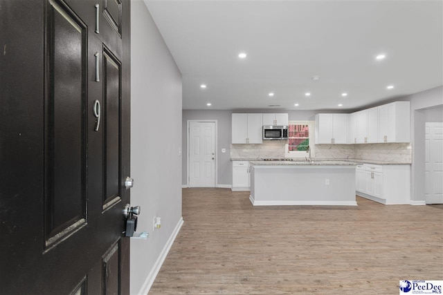 kitchen with tasteful backsplash, white cabinetry, a center island, light hardwood / wood-style floors, and light stone countertops