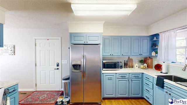 kitchen featuring blue cabinets, sink, light hardwood / wood-style floors, stainless steel appliances, and a textured ceiling